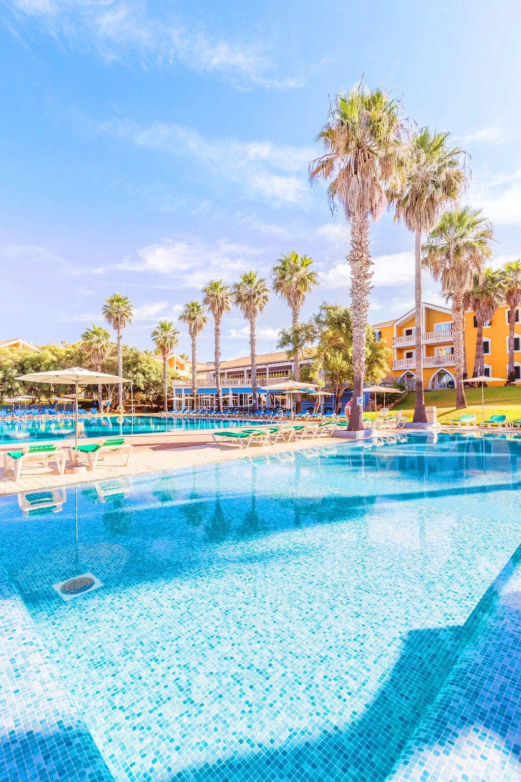 Un espace piscine comprenant plusieurs piscines, des palmiers et un bâtiment doté de balcons.