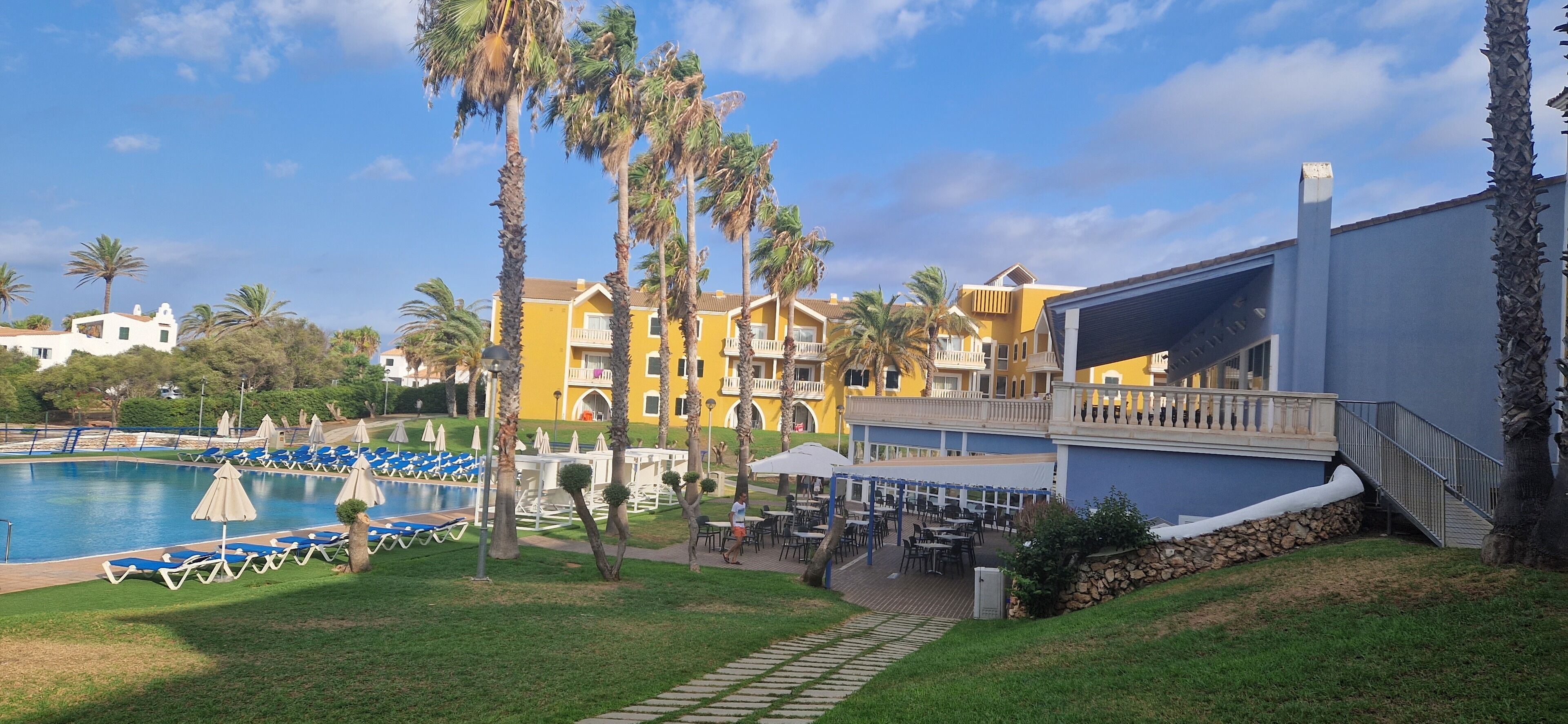 A resort with a swimming pool, palm trees, and outdoor seating areas.
