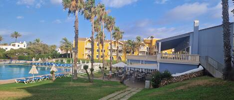 A resort with a swimming pool, palm trees, and outdoor seating areas.