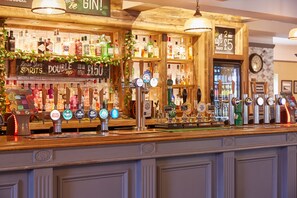 A bar area with a wooden counter, multiple beer taps, and shelves stocked with various bottles. - Corner House Hotel by Greene King Inns (Newcastle-upon-Tyne)