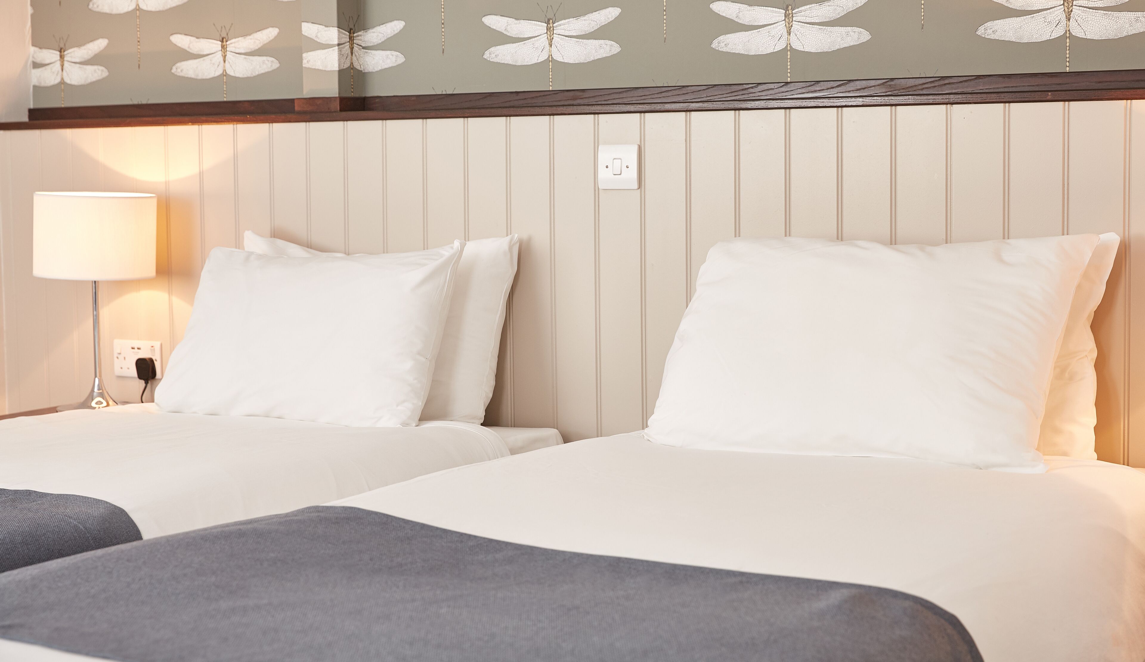 A hotel room with two beds, a nightstand with a lamp, and a wall with a dragonfly design.