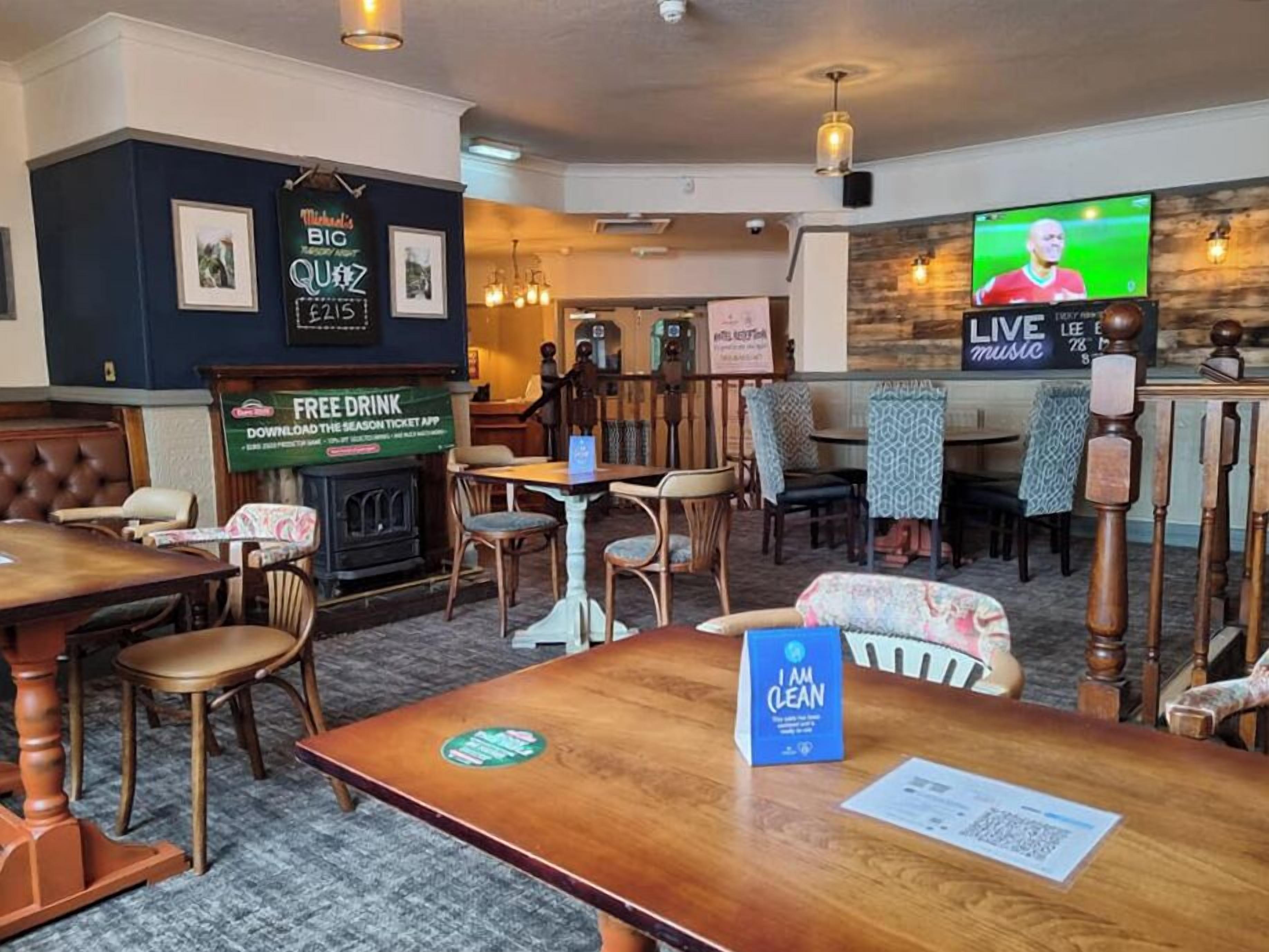 A restaurant interior with wooden tables and chairs, a fireplace, and a television displaying a sports event.