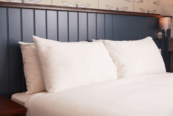 A neatly made bed with white linens and pillows, a wooden headboard, and a wall with butterfly wallpaper.