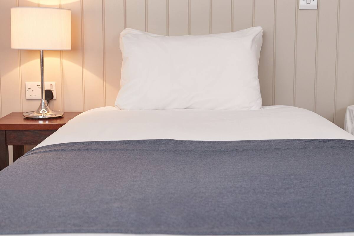 Une chambre d’hôtel avec un lit, une table de chevet avec une lampe et un mur orné d’un motif représentant des libellules.