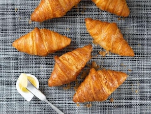 Four golden-brown croissants on a textured fabric surface with a lemon half and a spoon. - Super Namba Nipponbashi (Osaka)