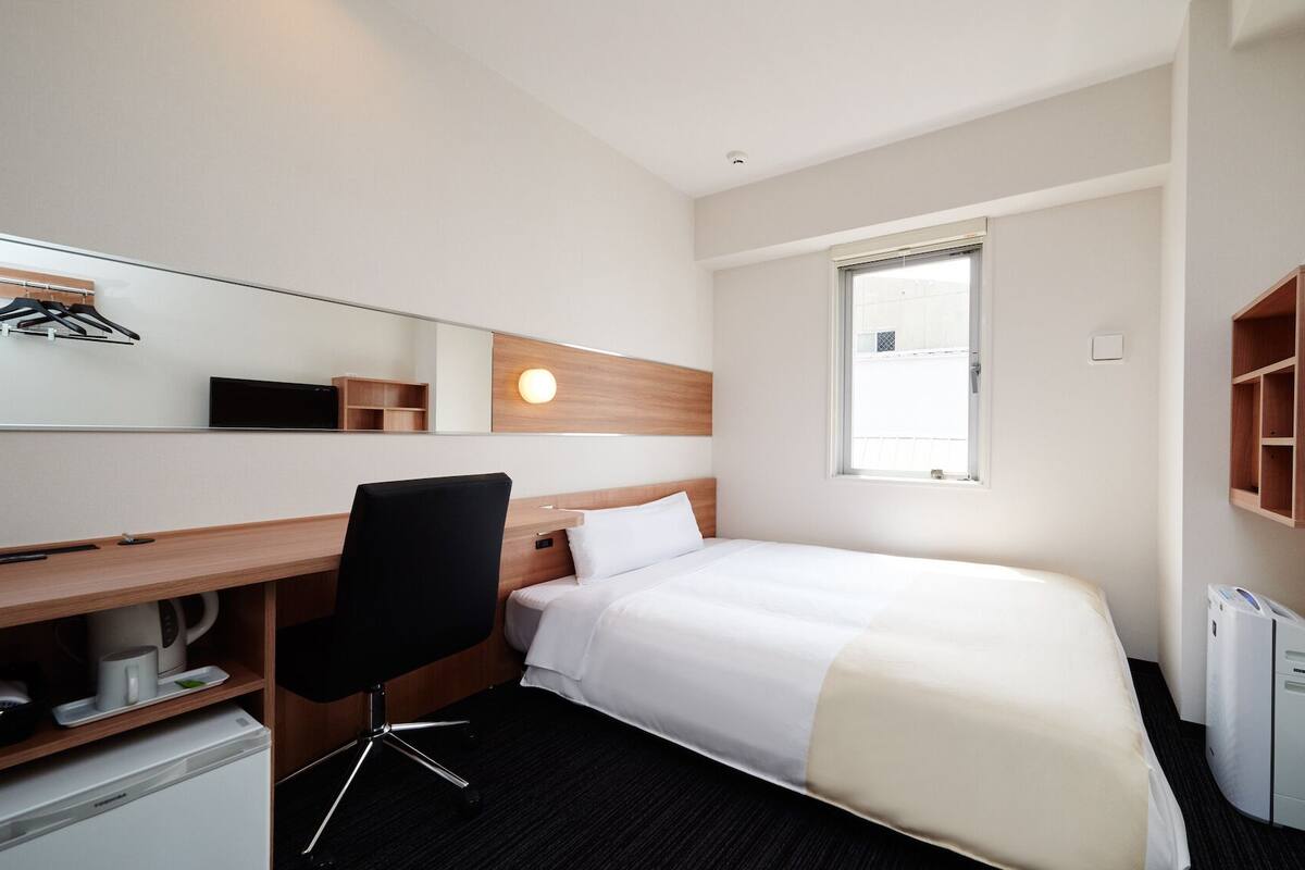 A hotel room with a bed, a desk, a chair, a television, and a window.