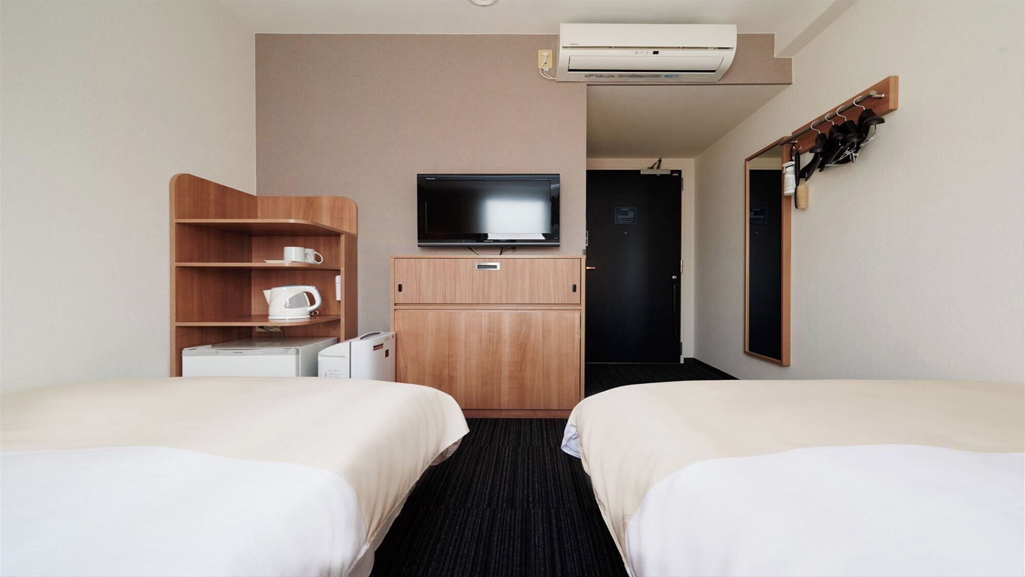 Habitació d'hotel amb dos llits, televisió, cafetera i un armari.