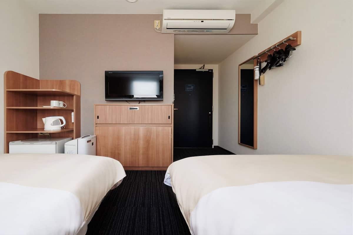A hotel room with two beds, a television, a coffee maker, and a wardrobe.
