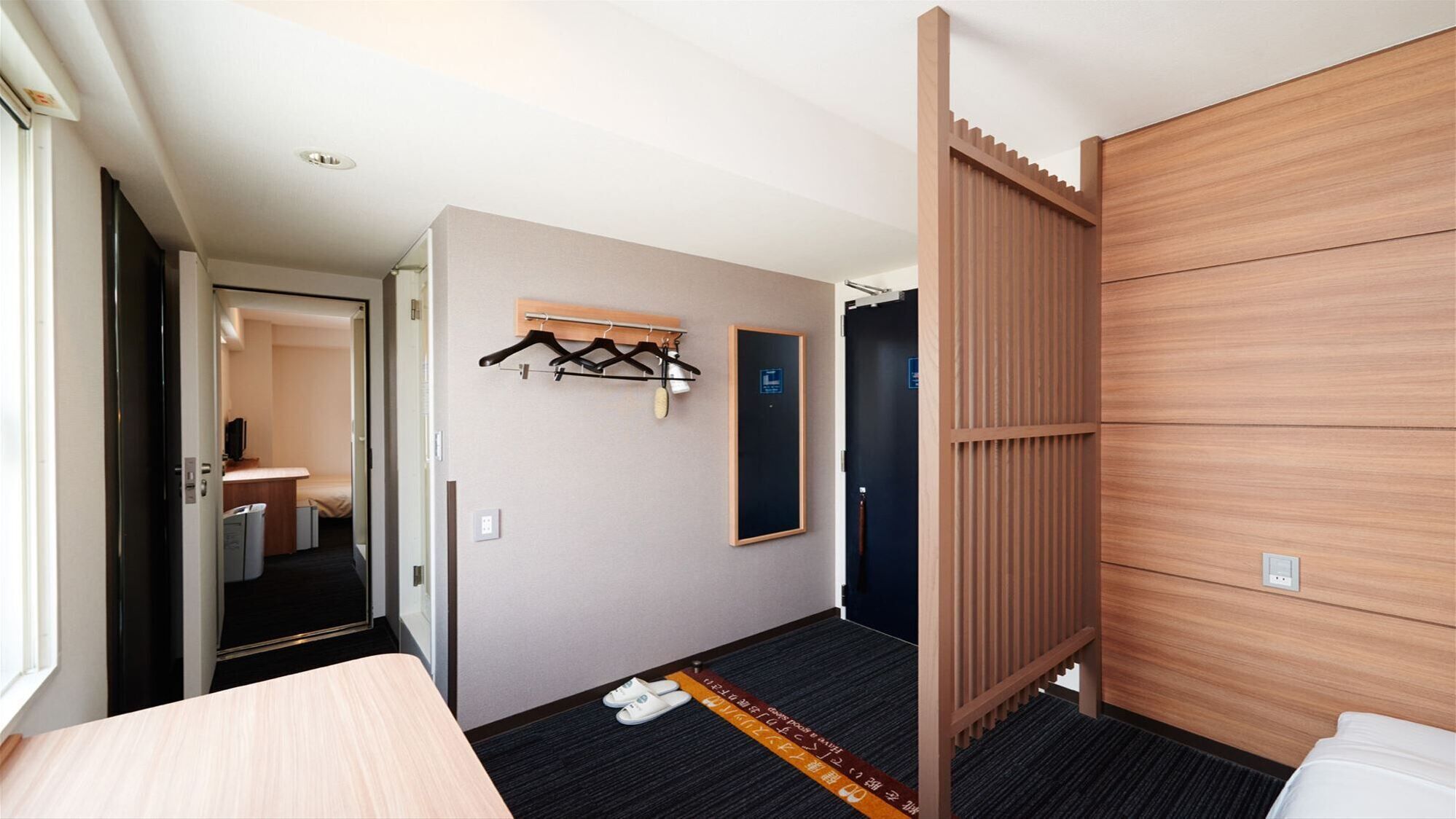 A hotel room with a bed, a desk, a coat rack, and a door leading to a bathroom.