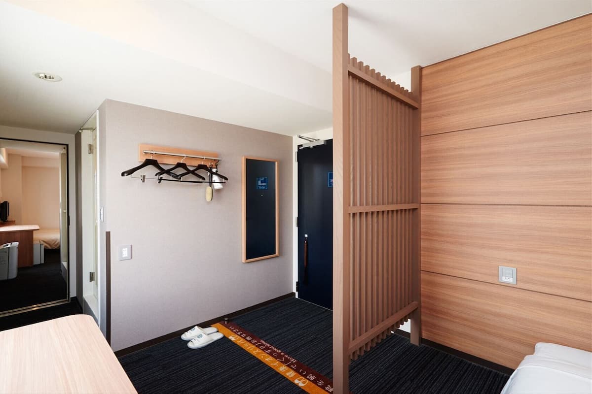 A hotel room with a bed, a desk, a coat rack, and a door leading to a bathroom.