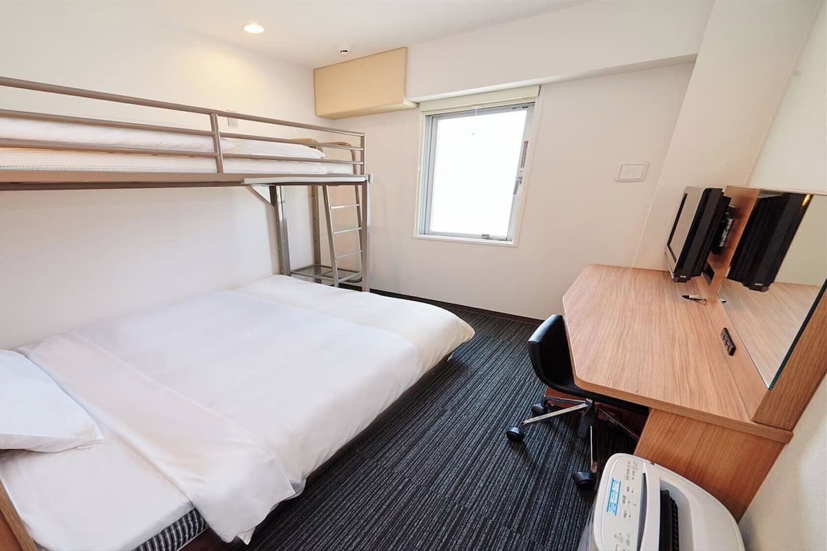 A bunk bed room with a desk, chair, and a television.