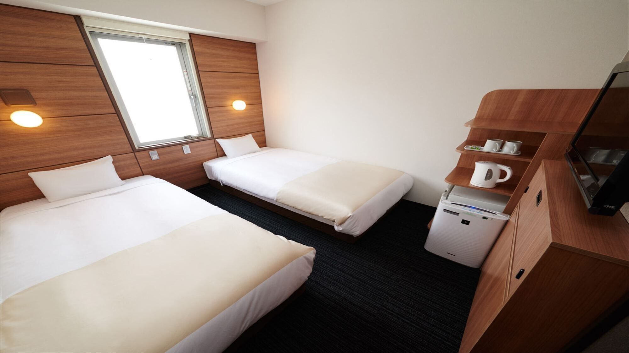 A hotel room with two beds, a window, a TV, and a coffee machine.