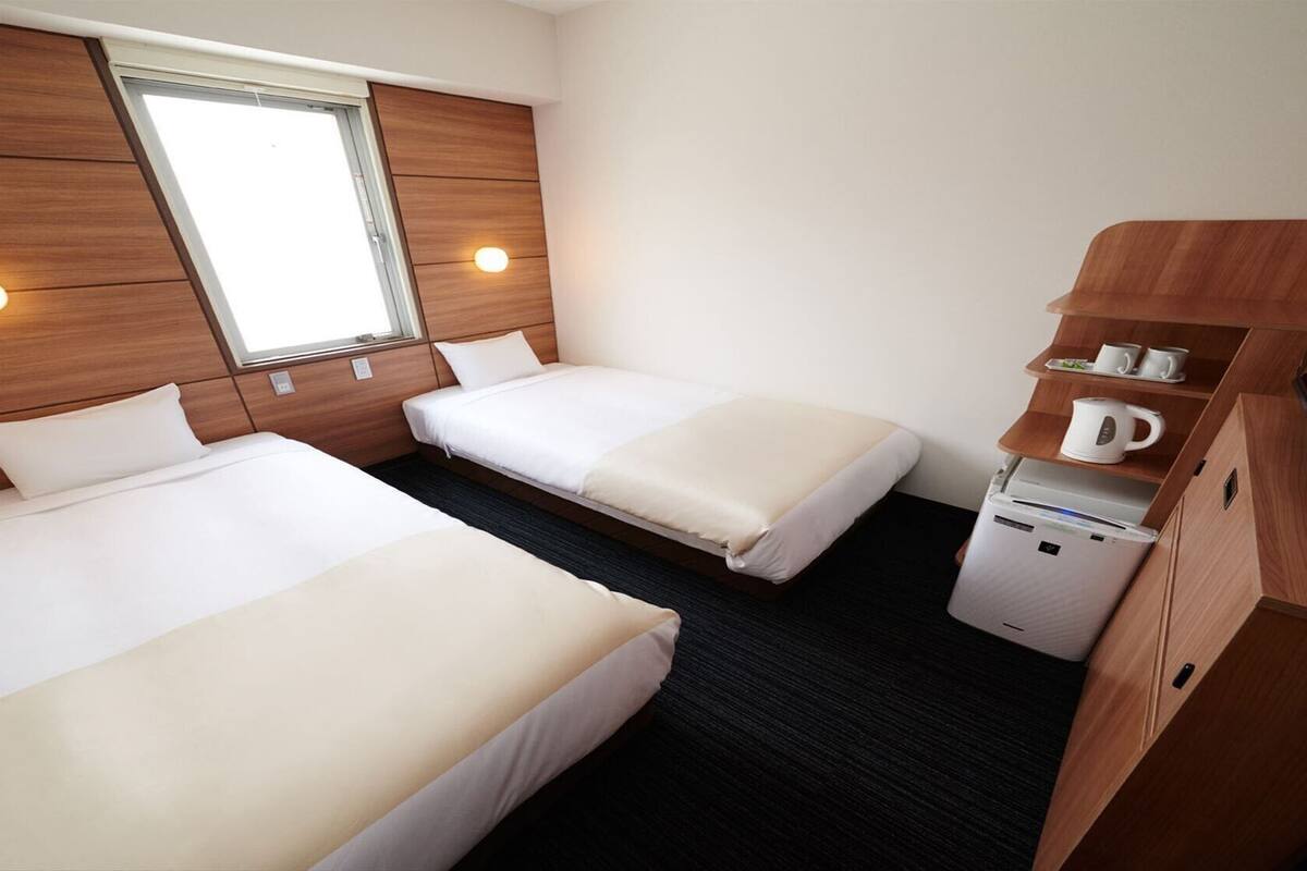 A hotel room with two beds, a window, a TV, and a coffee machine.