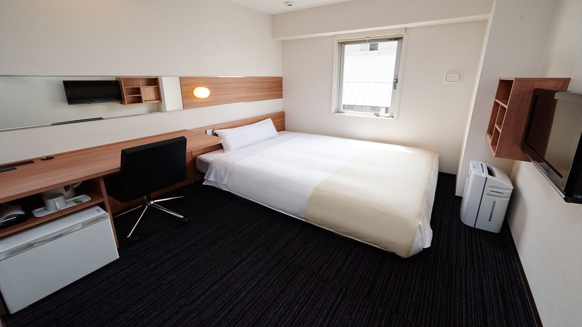 A hotel room with a bed, desk, TV, and a window.