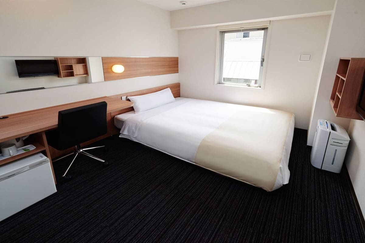 A hotel room with a bed, desk, TV, and a window.