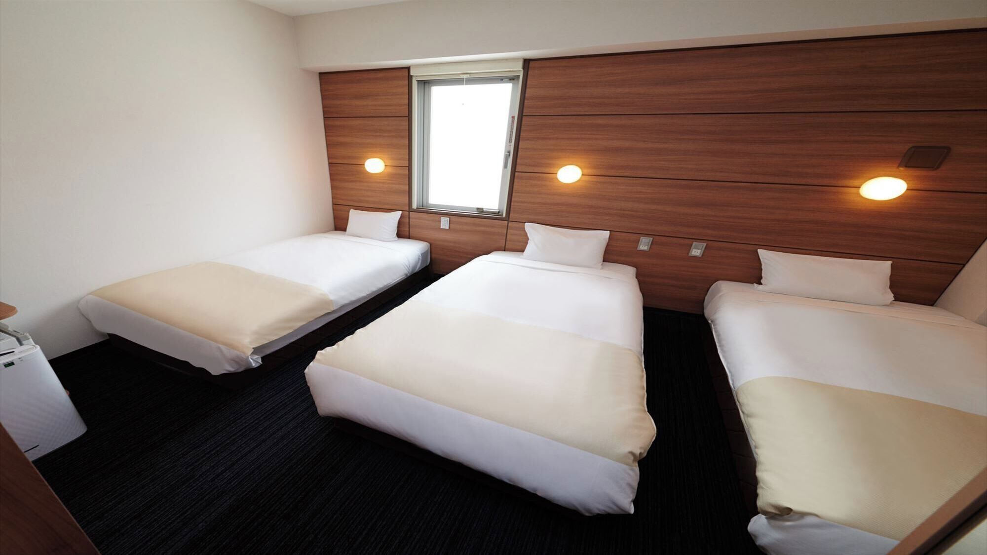 Habitació d'hotel amb tres llits, un escriptori petit i una finestra.