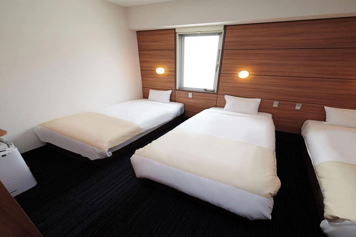 A hotel room with three beds, a small desk, and a window.