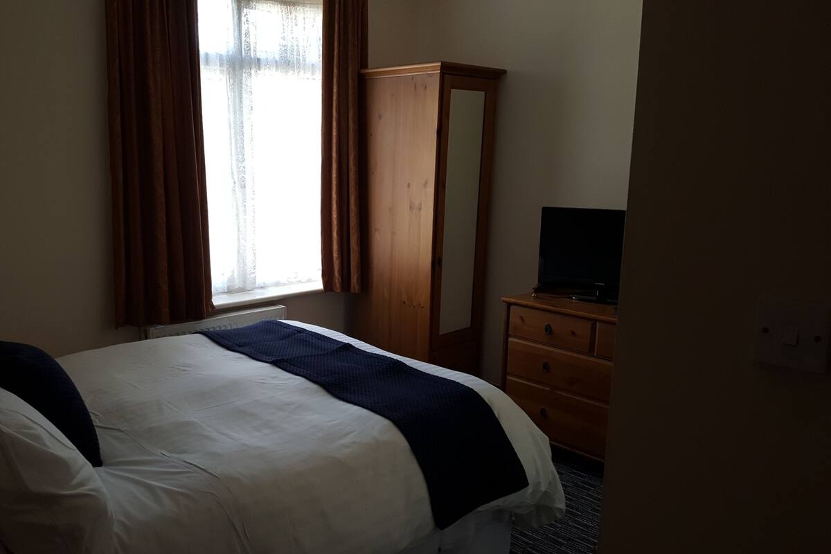 A hotel room with a bed, a dresser, a television, and a window with curtains.
