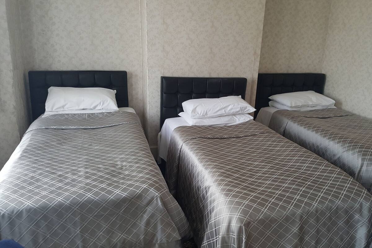 Three single beds with headboards, arranged in a row against a wall with a subtle floral pattern.
