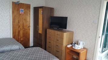 Un dormitorio con dos camas, un armario, un televisor y una mesita con una tetera y tazas.
