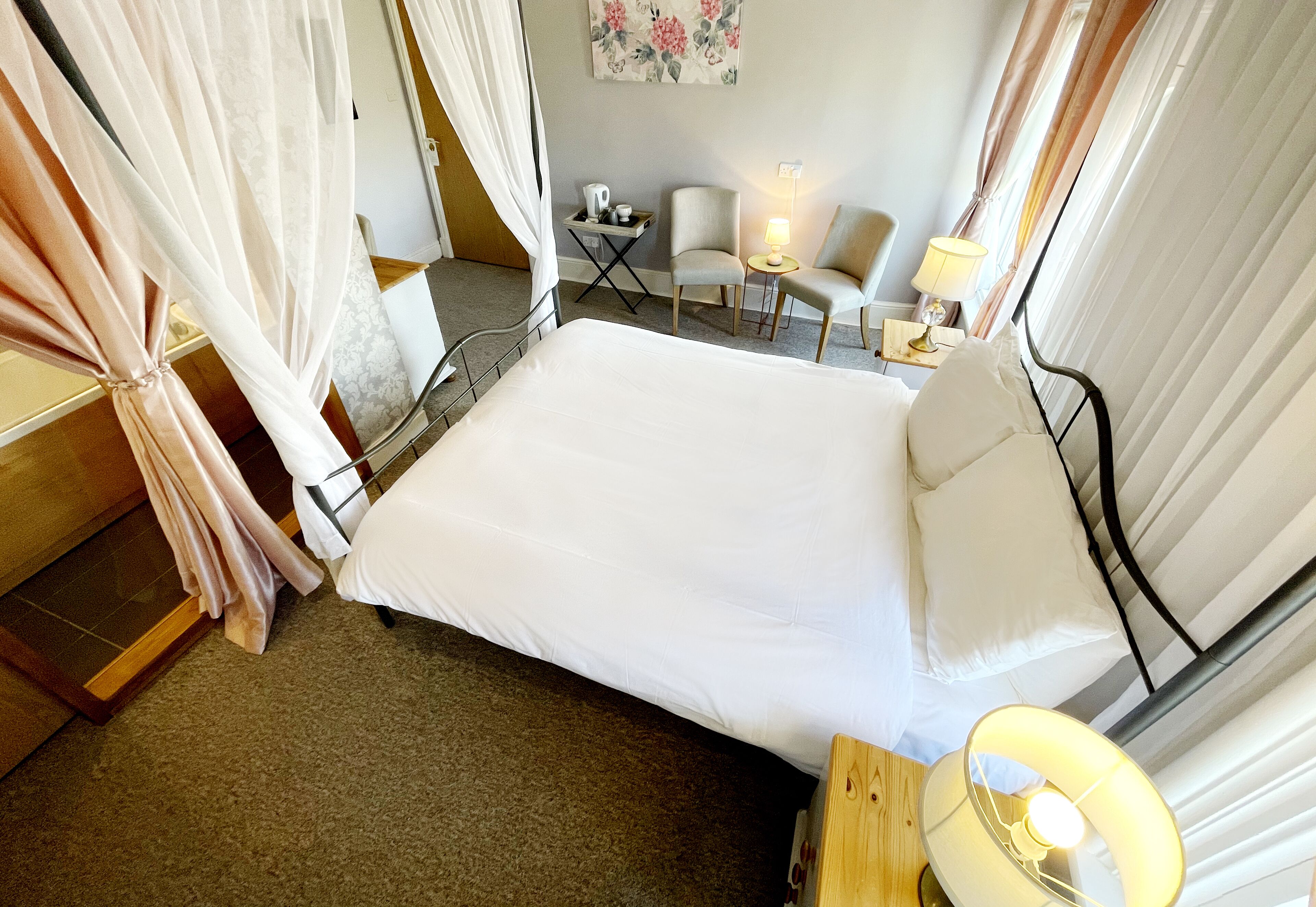 A neatly arranged hotel room with a bed, a small table with a lamp, two chairs, and a side table with a lamp.