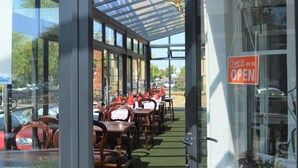 An outdoor cafe with tables and chairs, a glass enclosure, and a 'Come in we're open' sign. - Dukes Folly Hotel (Southport)