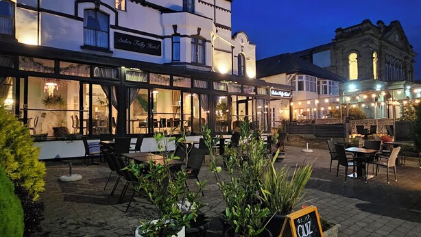 A historic building with a sign 'Dukes Folly Hotel' and outdoor seating area with tables and chairs. - Dukes Folly Hotel (Southport)