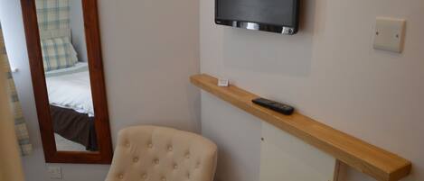 A hotel room with a bed, a chair, a television mounted on the wall, and a shelf with a remote control.