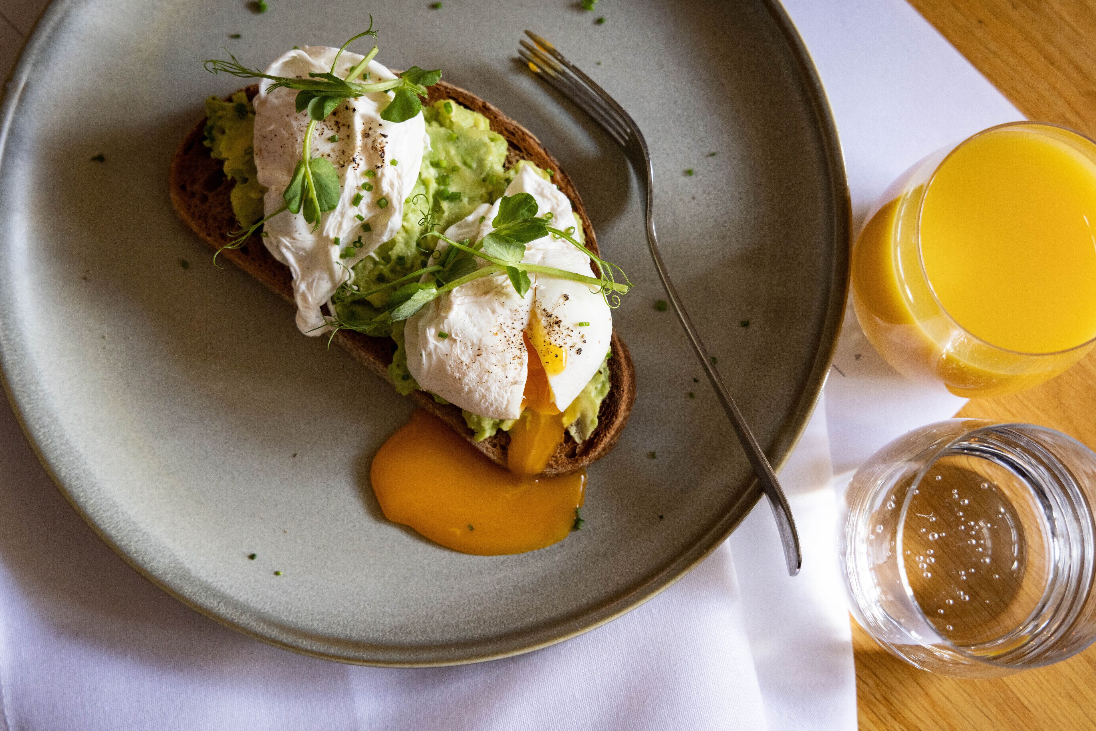 A plate with a poached egg, avocado, and greens on toast, accompanied by a glass of orange juice.