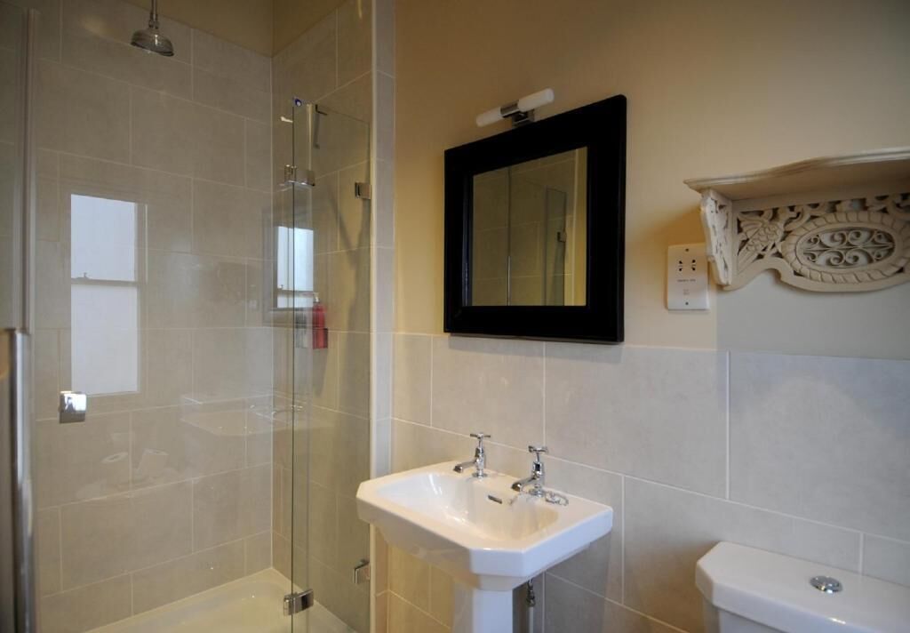 Ein Badezimmer mit Duschkabine aus Glas, einem weißen Waschbecken mit zwei Wasserhähnen und einer Toilette.