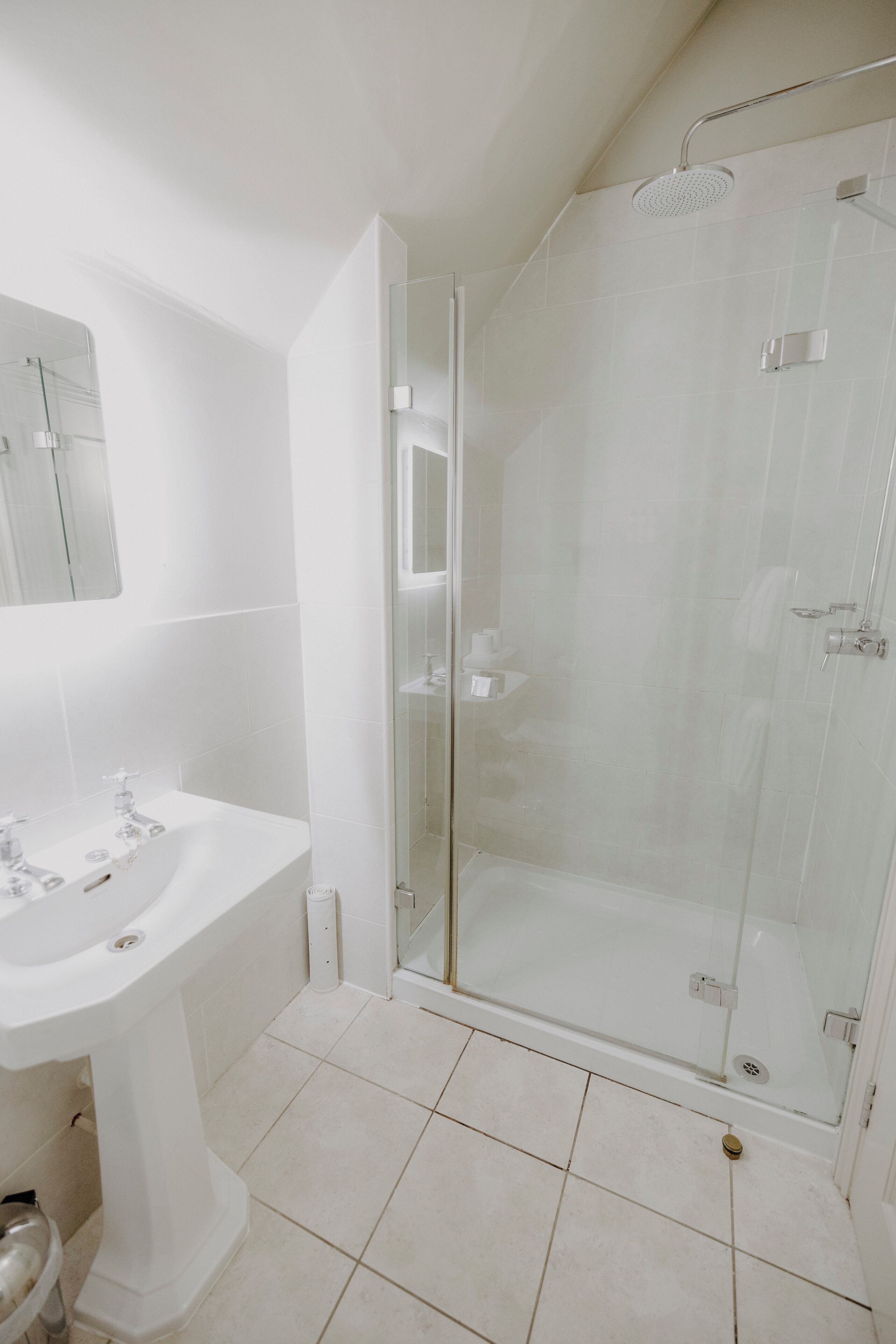 A modern bathroom with a glass-enclosed shower, a pedestal sink, and a mirror above the sink.
