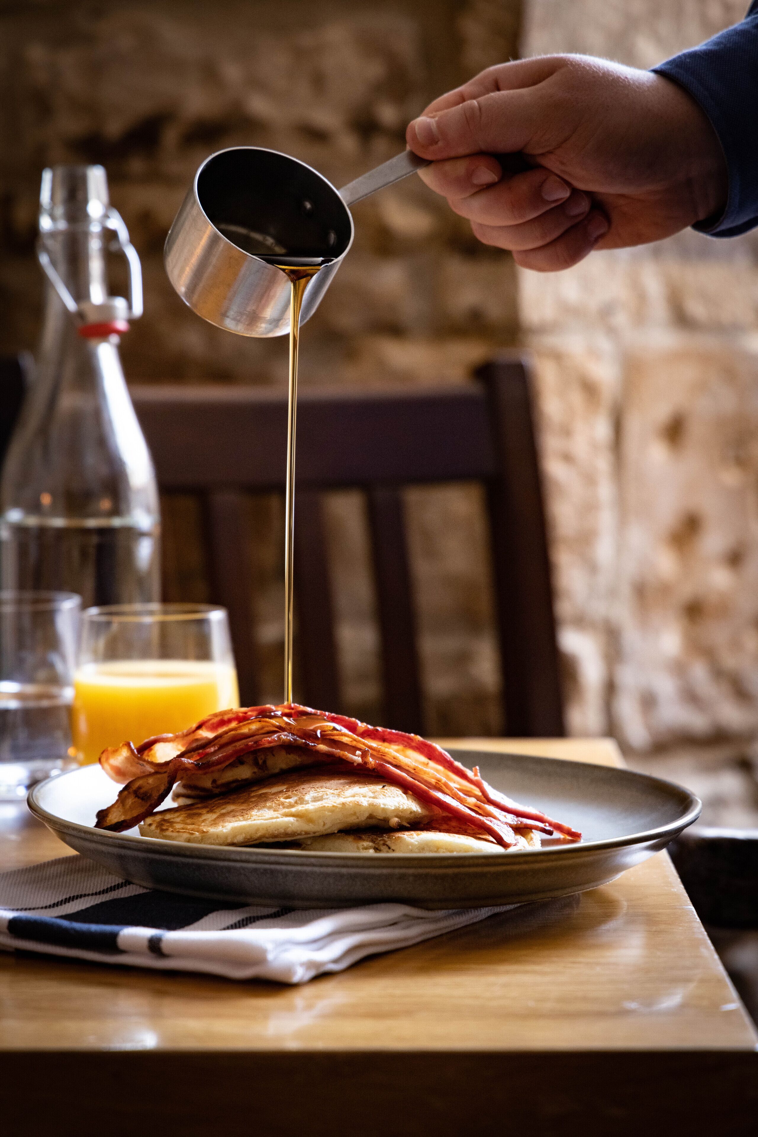 A plate of food with a hand pouring syrup over it.