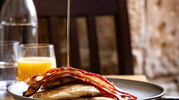 A plate of food with a hand pouring syrup over it.