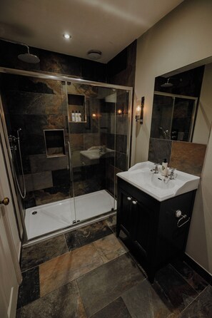 A modern bathroom with a glass-enclosed shower, a white sink, and a dark-toned vanity. - The Bull And Swan (Stamford)