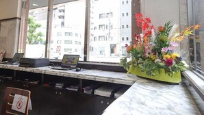 A reception desk with computers, a flower arrangement, and a view of buildings through large windows.