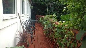 Una terraza de madera con una mesa y sillas, rodeada de macetas con plantas y una celosía roja.