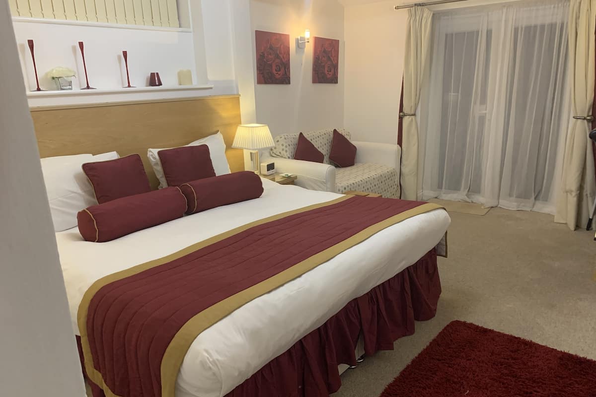 A hotel room with a large bed, a bedside table, a lamp, a chair, and a window with curtains.