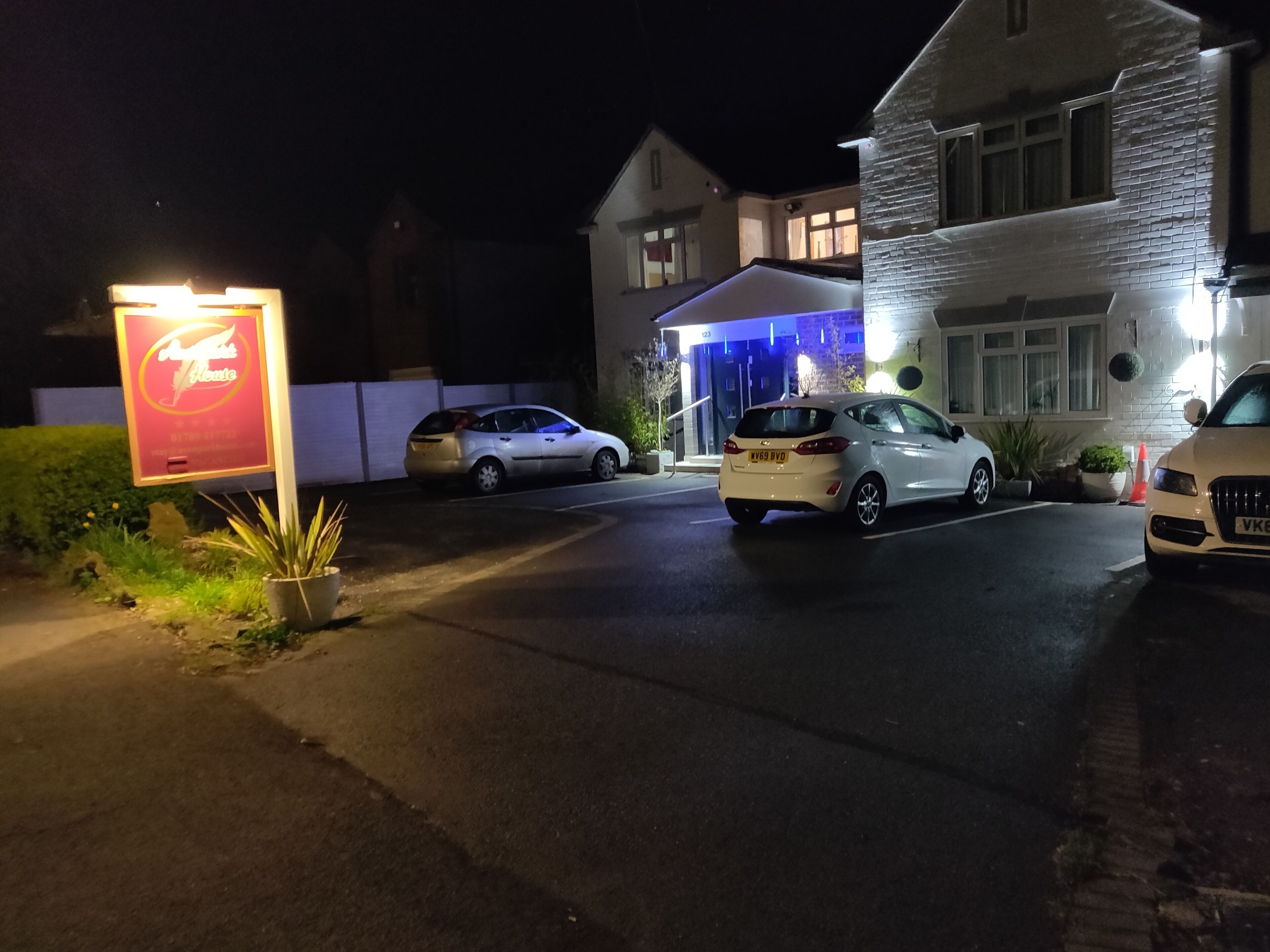 Entrada de hotel con letrero, coches estacionados y un edificio de fachada de piedra.