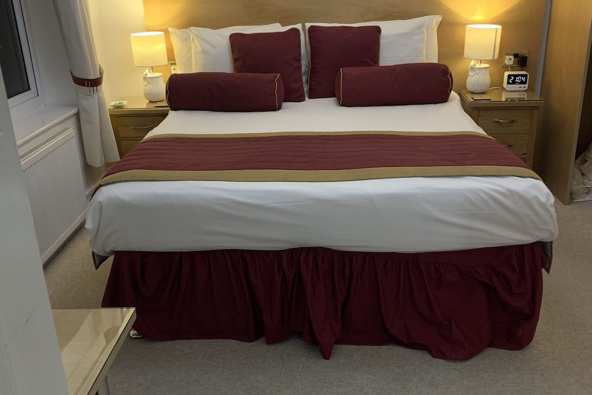 A neatly made bed with a white and maroon bedspread, two red rose paintings on the wall, and bedside lamps.