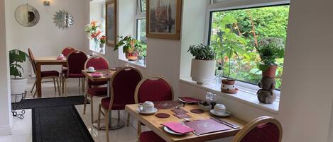 Un comedor con una mesa larga, sillas tapizadas en rojo y plantas en macetas en el alféizar.