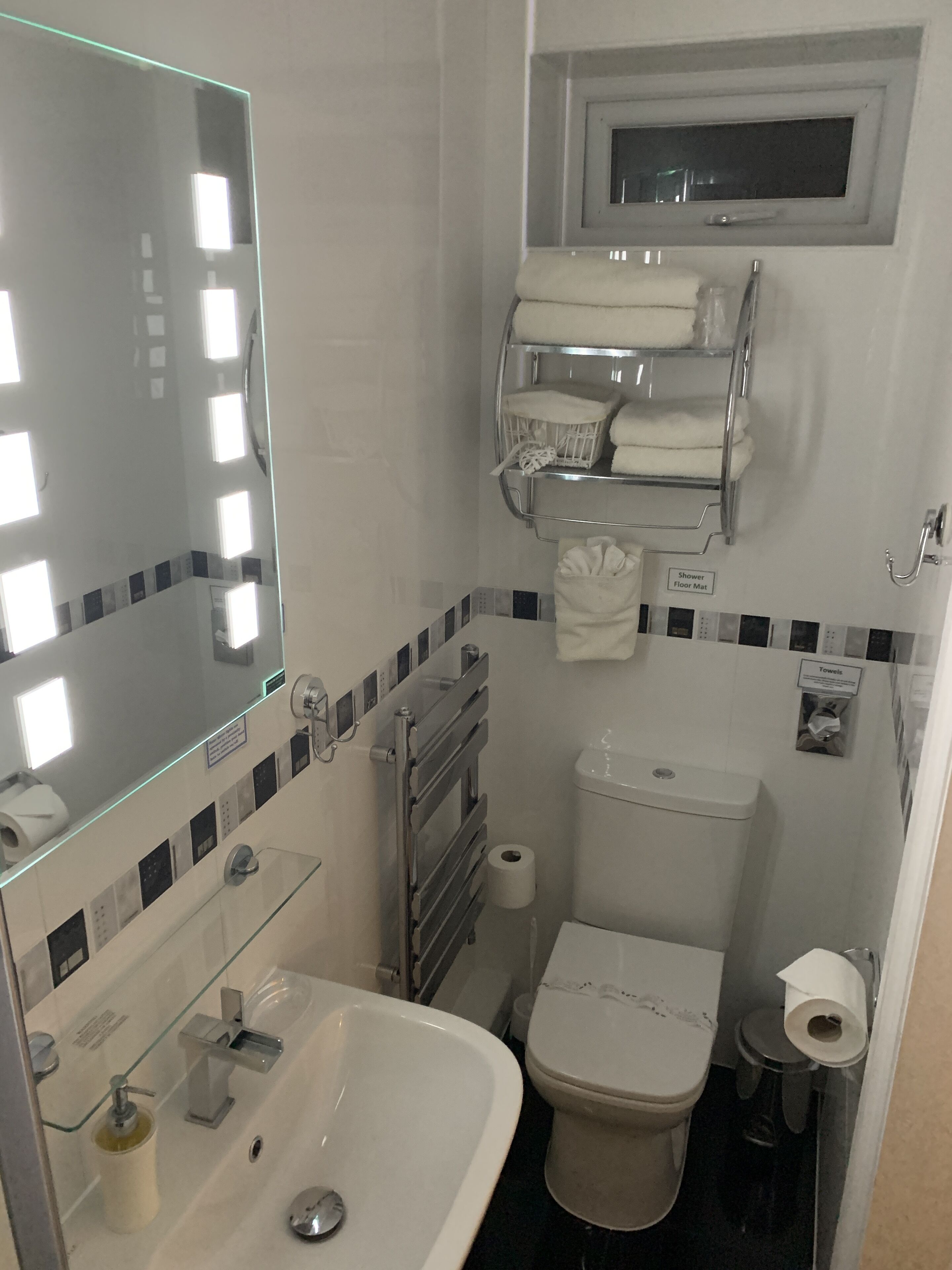 A compact bathroom with a sink, toilet, and a mirror. There are towels and a shower mat visible.