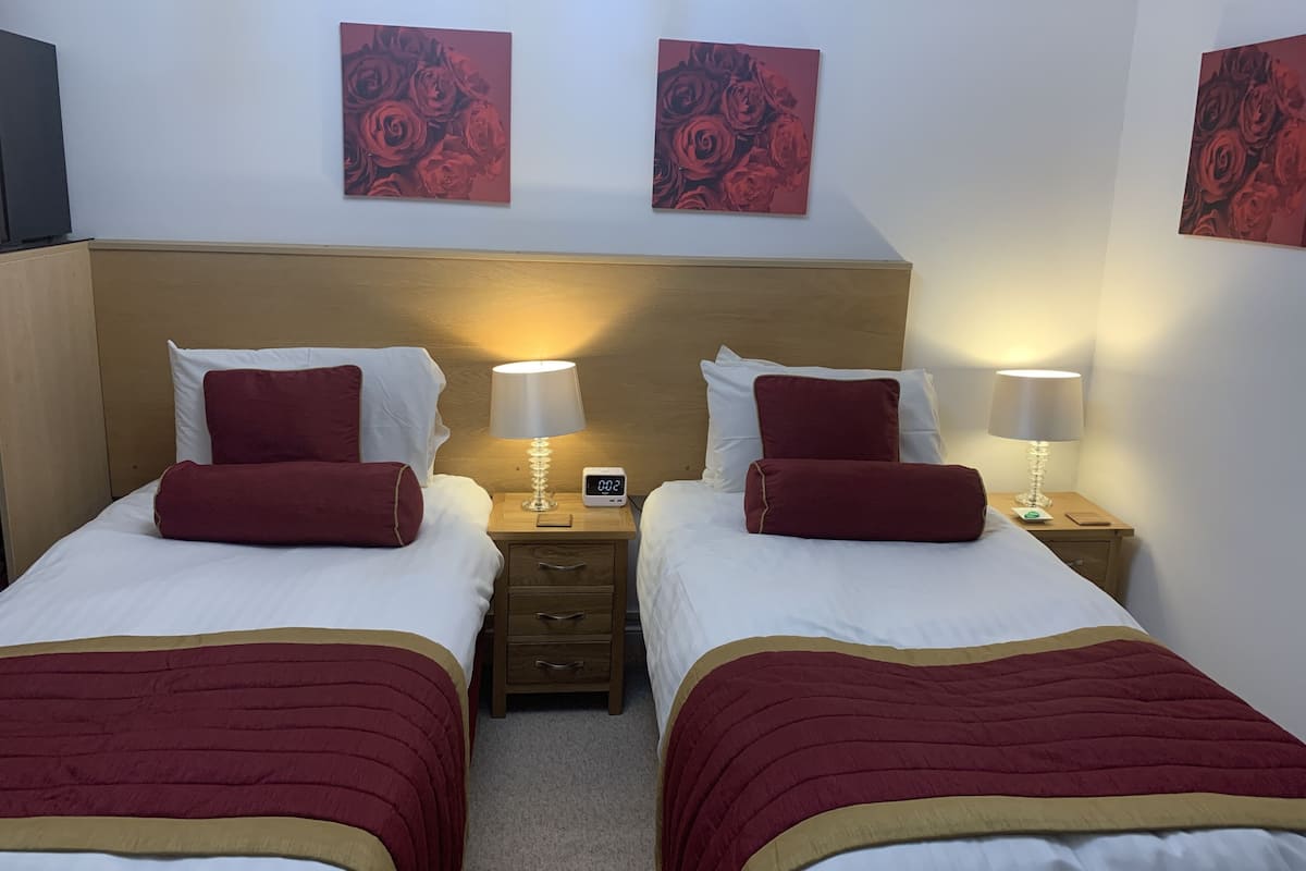 A hotel room with two beds, each with a red and white bedspread, two bedside lamps, a wooden headboard, and two red floral wall art pieces.