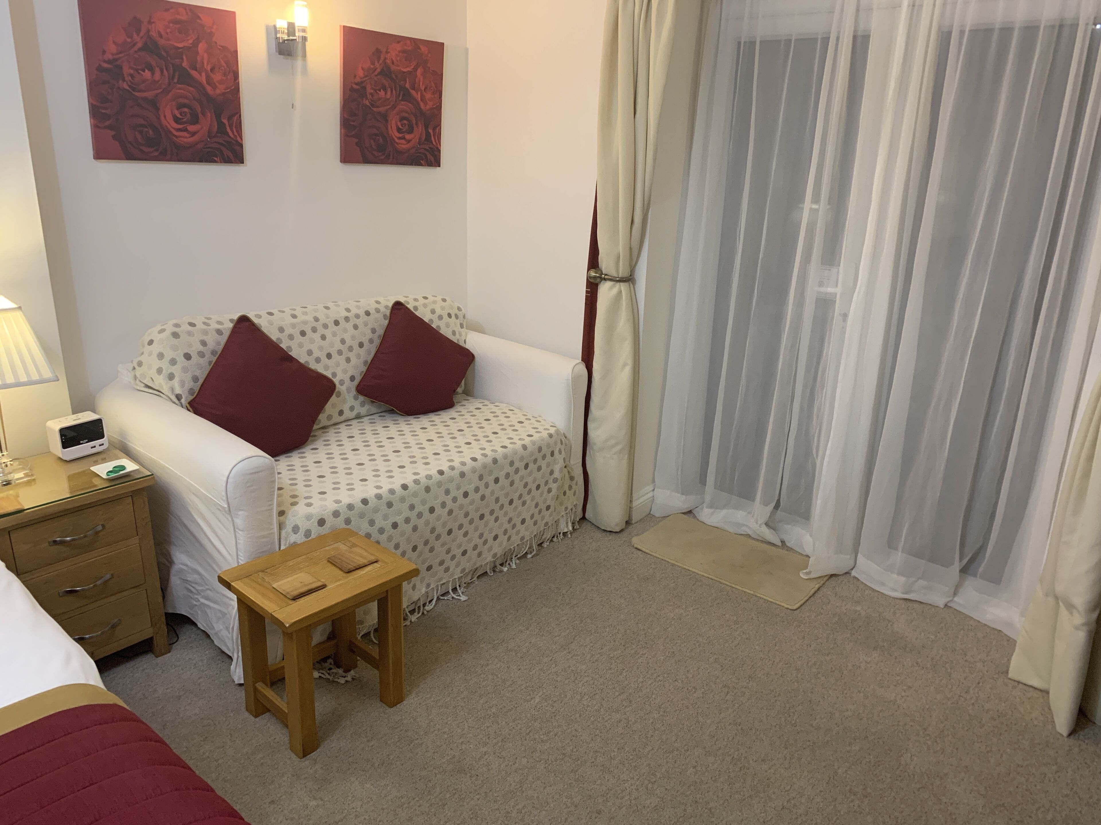 Een gezellige kamer met een witte bank, twee rode kussens, een klein houten tafeltje en een lamp.