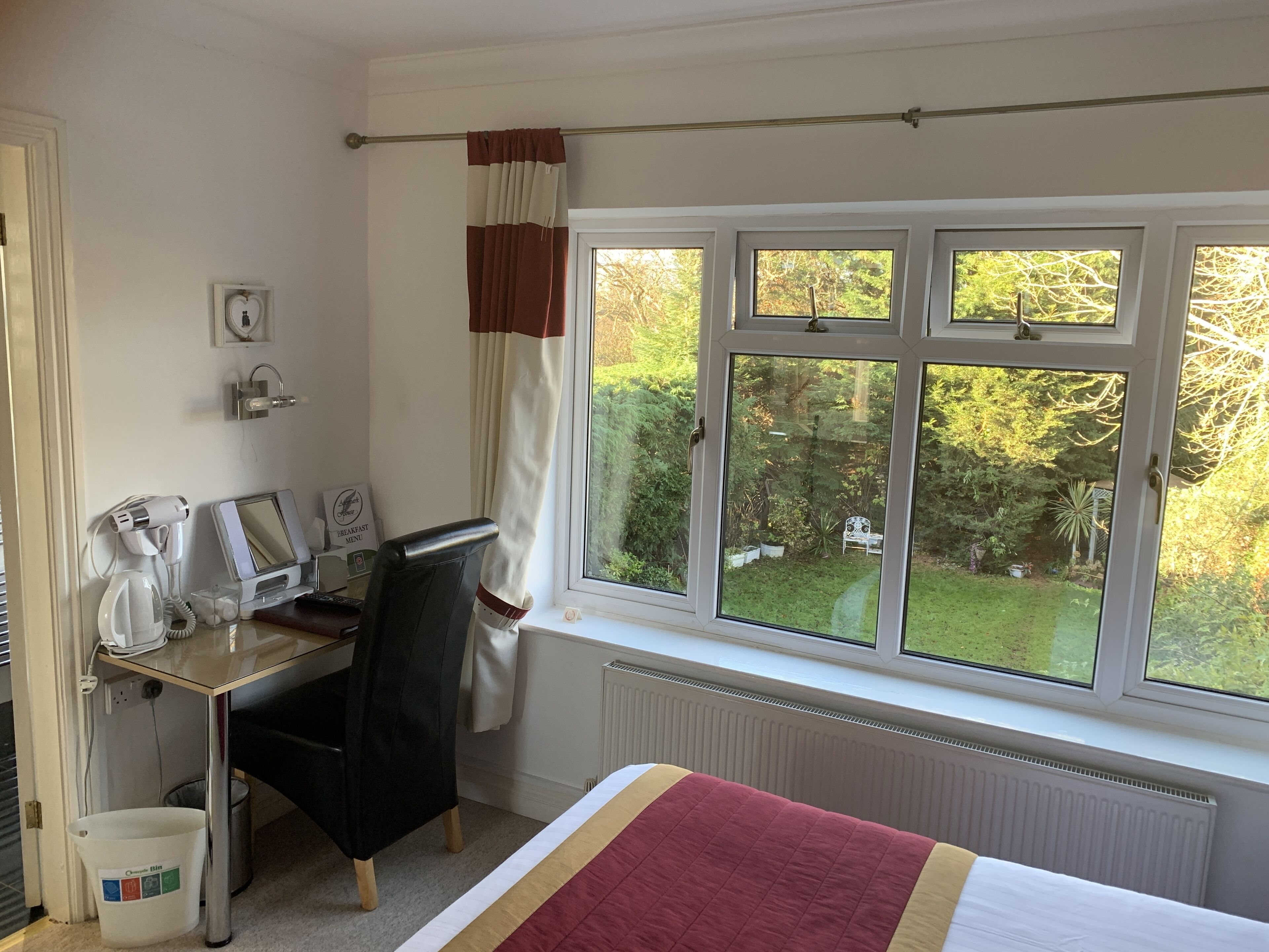A hotel room with a bed, a desk with a computer, a hairdryer, and a bucket.