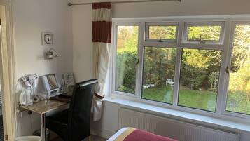 A hotel room with a bed, a desk with a computer, a hairdryer, and a bucket.