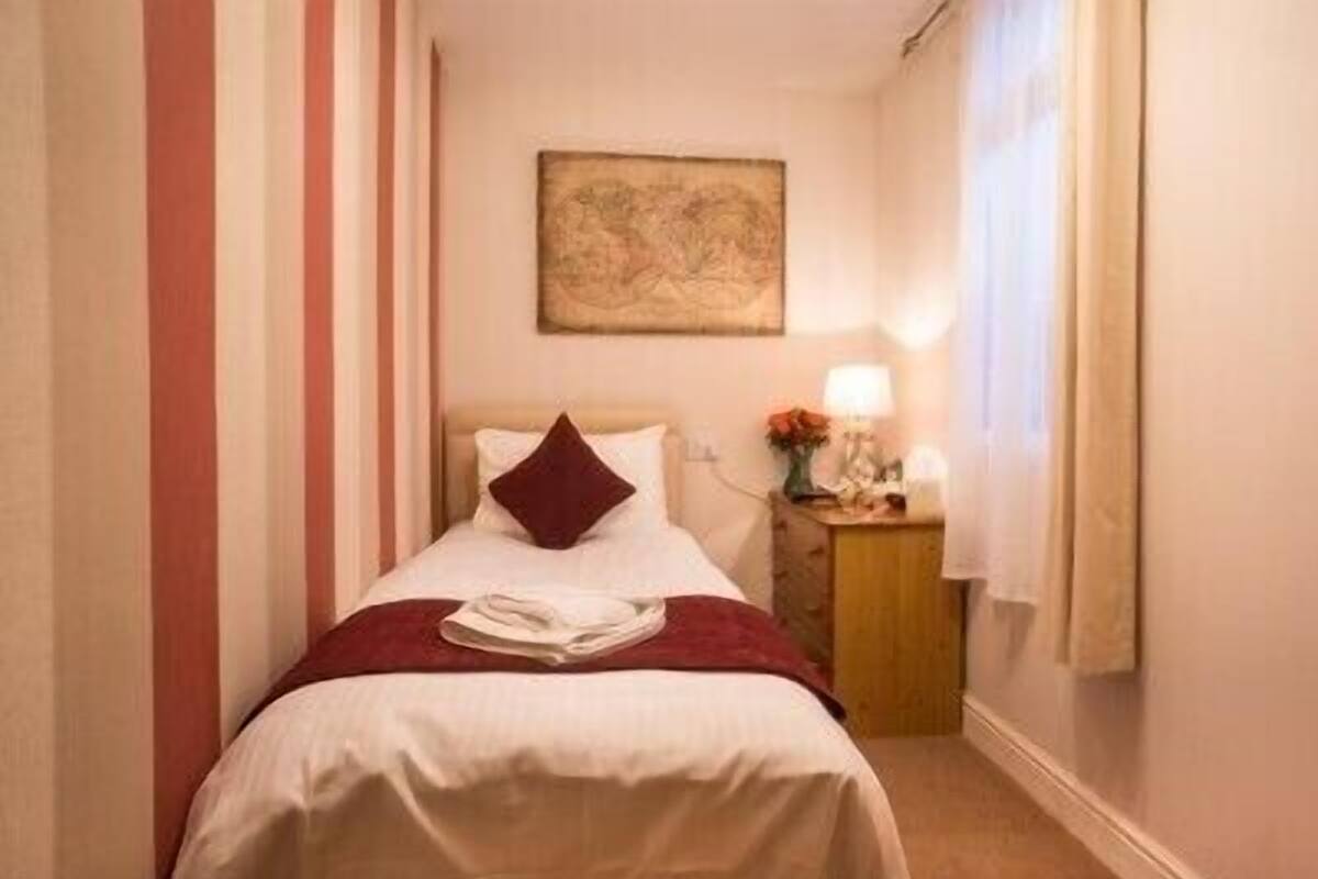 A hotel room with a bed, a nightstand with a lamp, and a painting on the wall.