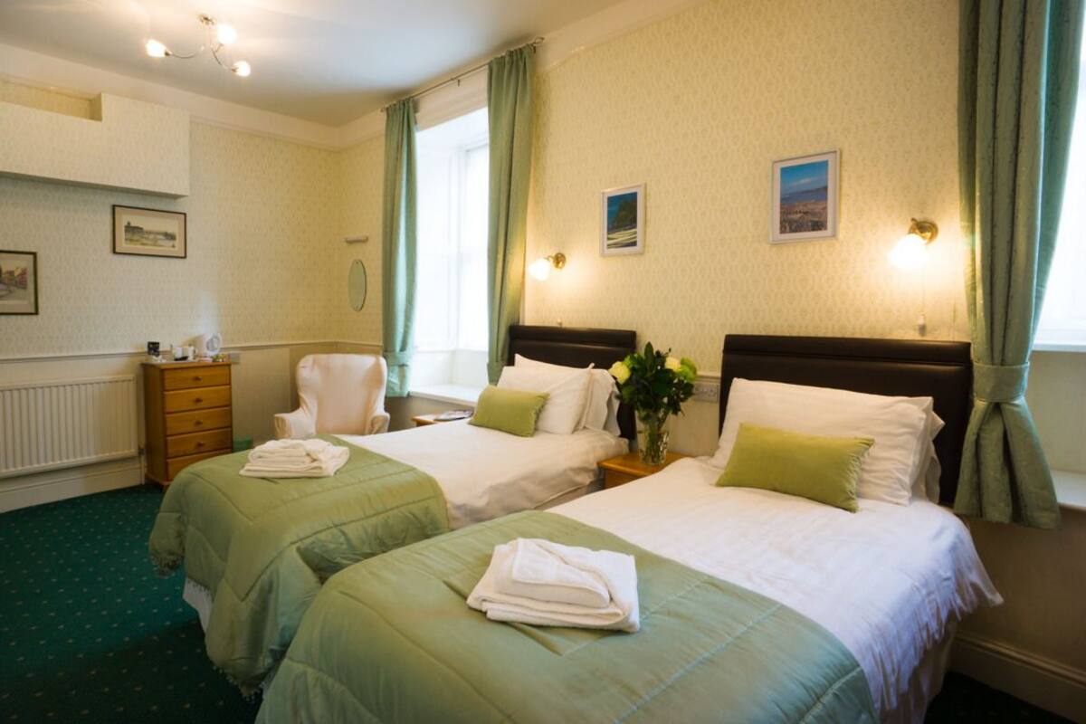 A hotel room with two beds, a chair, a dresser, and a radiator.