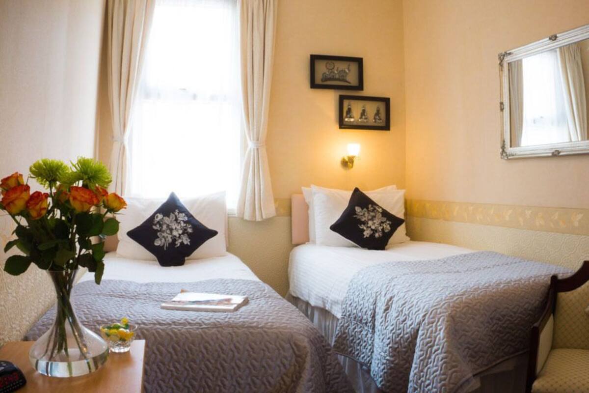A hotel room with two beds, a vase with flowers, a bedside table, and a mirror on the wall.