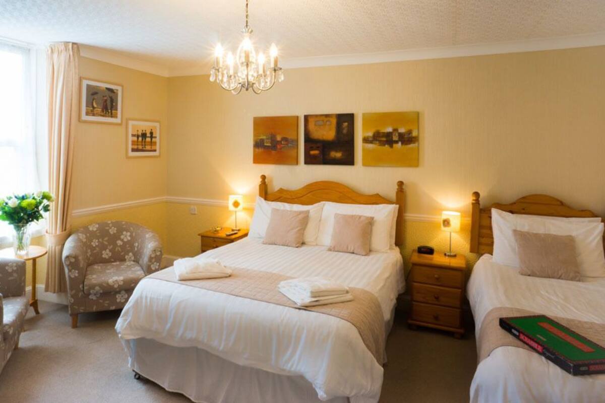 A hotel room with two beds, a chair, a nightstand, and a chandelier.