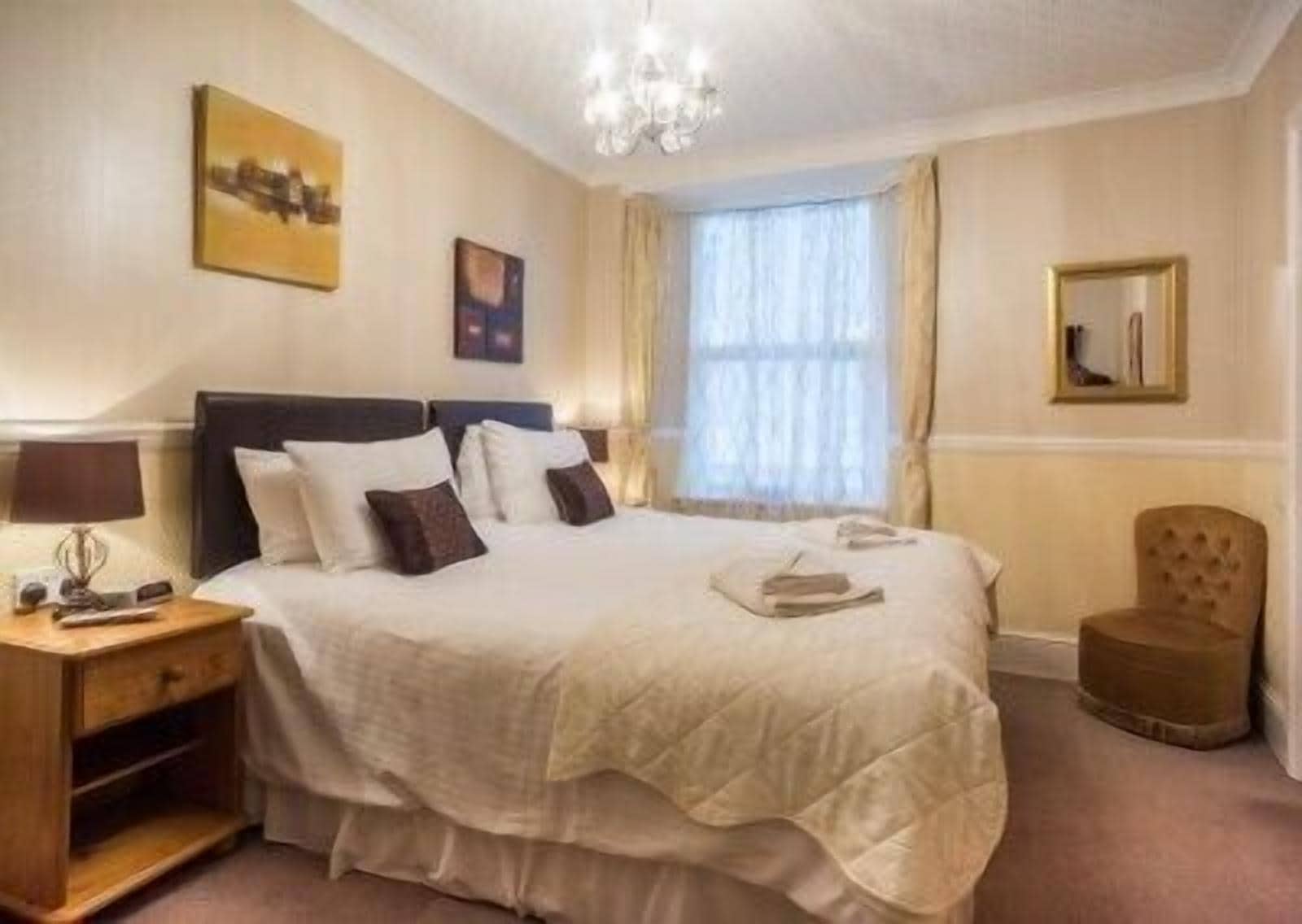 A hotel room with a large bed, a nightstand, a chair, and a chandelier.